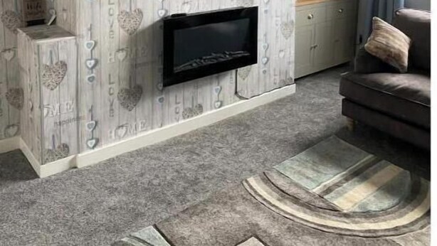 A living room with a flat-screen TV mounted above a fireplace, a sofa, and patterned wallpaper. - Birdsong View - comfortable apartment in Amble (Amble)