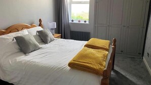 A bedroom with a bed, pillows, a lamp, a window, and a wardrobe.