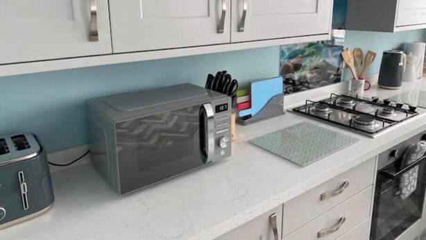 A modern kitchen with white cabinets, a gas stove, a microwave, and a toaster.