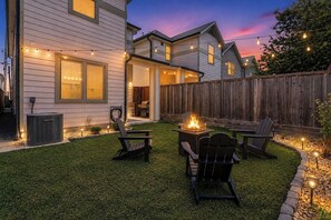 Ein Garten mit Feuerstelle, Sitzgelegenheiten im Freien und Lichterketten.