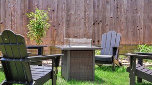 A patio with Adirondack chairs and a square table, set against a wooden fence. - 4BR Houston Heights - 15 Mins to Downtown (Houston)