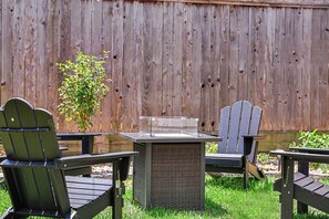 Un patio con sillas Adirondack y una mesa cuadrada, frente a una valla de madera.