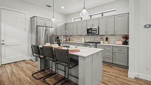 A modern kitchen with grey cabinets, stainless steel appliances, a central island with bar stools, and pendant lighting. - 4BR Houston Heights - 15 Mins to Downtown (Houston)