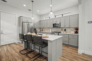 Una cocina moderna con armarios grises, electrodomésticos de acero inoxidable, una isla central con taburetes altos y luces colgantes.