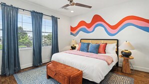 A hotel room with a bed, curtains, a ceiling fan, a wall mural, bedside lamps, and a bench. - 4BR Houston Heights - 15 Mins to Downtown (Houston)