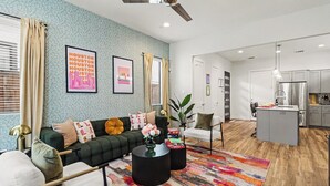 A modern living room with a sofa, coffee table, and a colorful rug. There is a kitchen area with a refrigerator and a dining table. - 4BR Houston Heights - 15 Mins to Downtown (Houston)