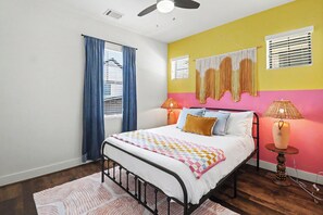Une chambre à coucher avec un lit, deux lampes de chevet, un ventilateur de plafond et une fenêtre avec des rideaux.