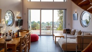 A spacious living area with a wooden dining table, a sofa, and a large sliding glass door leading to an outdoor balcony. - Villa Milos - Three Bedroom Villa, Sleeps 6 (Lefkada)