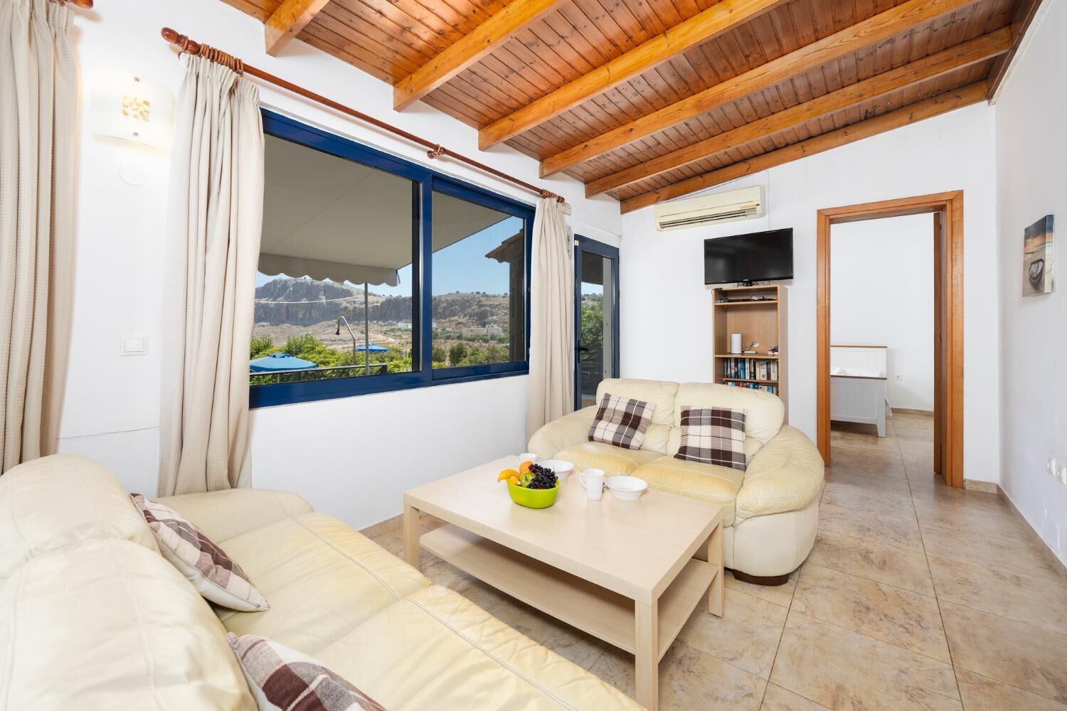 A cozy living room with a sofa, a coffee table, and a view of a mountainous landscape through a large window.