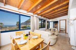 A dining area with a table set for two, a sofa, and a view of the sea.