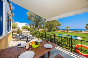 A balcony with a table set for two, a bottle of wine, and a bowl of fruit.