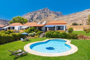 A residential property with a swimming pool, a covered patio, and a mountainous backdrop.