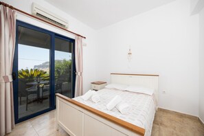 A bedroom with a bed, a nightstand, a window with curtains, and an air conditioning unit.