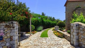 A stone pathway leading to a building with a stone wall on one side and a lush garden on the other. - Panorama II Villas - Two Bedroom Villa, Sleeps 7 (Ditiki Mani)