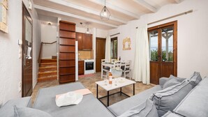 A modern living room with a sofa set, a dining table with chairs, a kitchen area with a stove and cabinets, and a staircase leading to another level. - Panorama II Villas - Two Bedroom Villa, Sleeps 7 (Ditiki Mani)