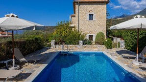 A stone building with a pool, surrounded by greenery and umbrellas. - Panorama II Villas - Two Bedroom Villa, Sleeps 7 (Ditiki Mani)
