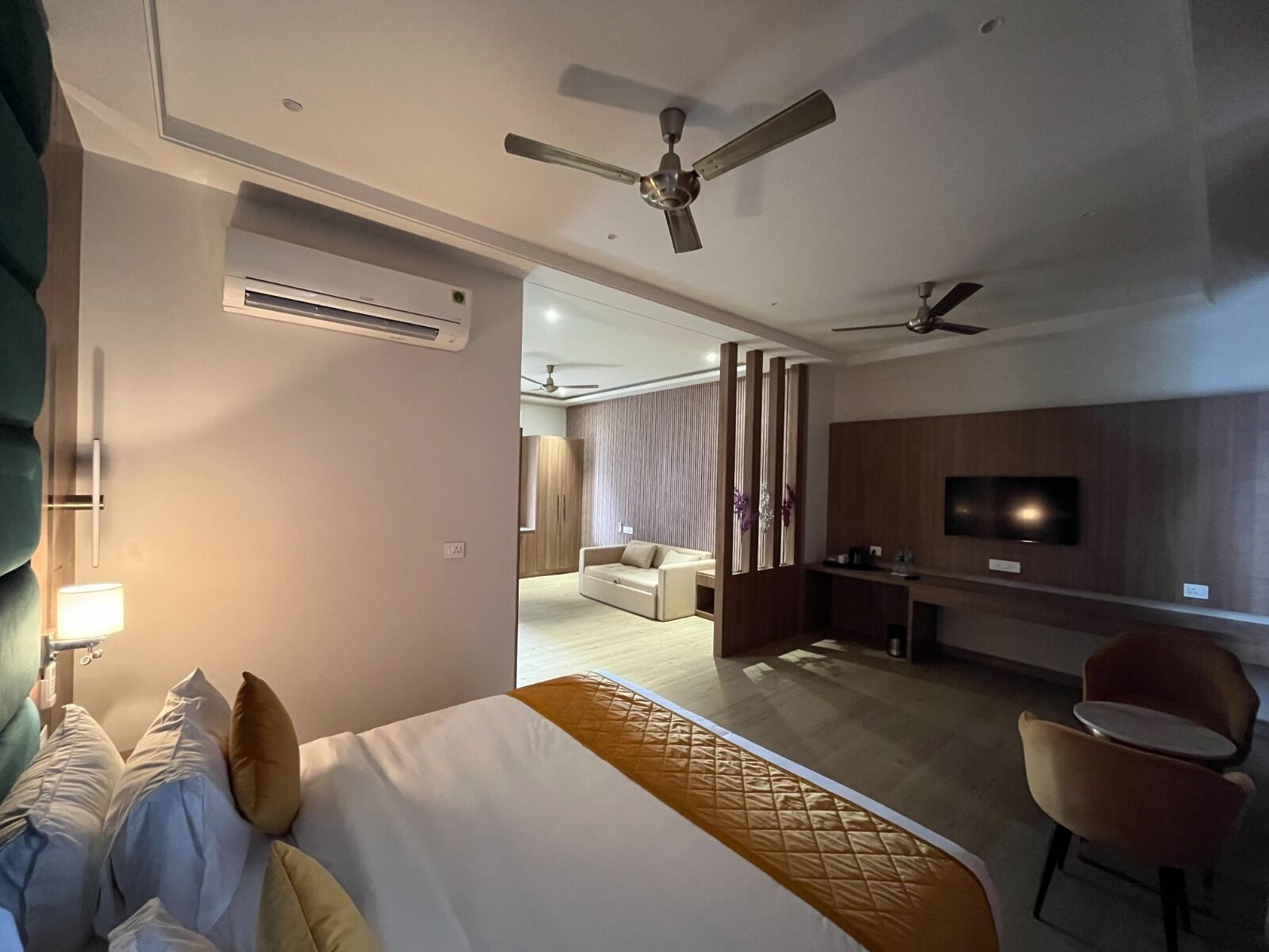 Habitació d'hotel amb llit, escriptori, televisió, cadira i ventilador de sostre.