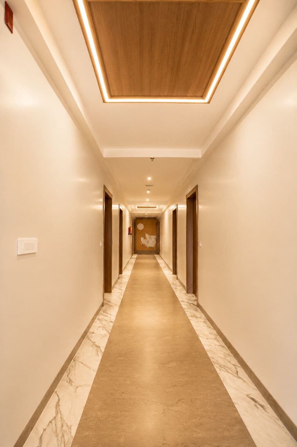 Un couloir d’hôtel avec un sol en marbre, un plafond en bois et des portes de part et d’autre.