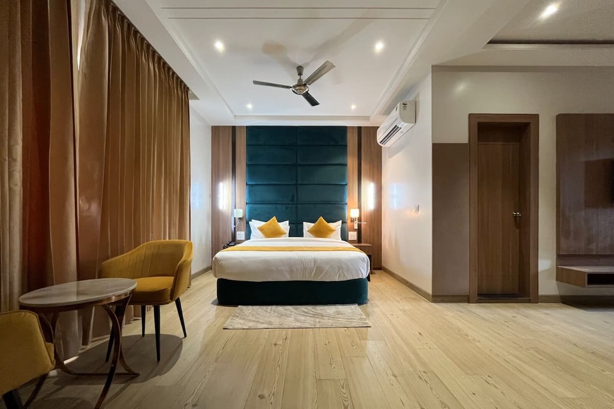 Camera d'albergo con un letto grande, una ventola a soffitto, un pavimento in legno e un tavolino con due sedie.