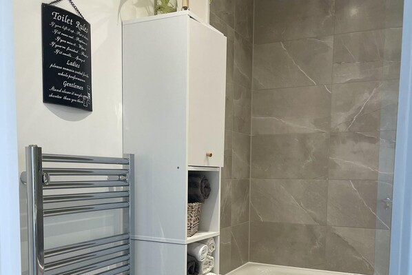 Une salle de bain équipée d’un porte-serviettes, d’un meuble contenant des serviettes et d’un panneau indiquant les règles d’utilisation des toilettes.