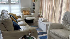 Ein Wohnzimmer mit einem beigefarbenen Sofa, einem weißen Sessel und einem kleinen Tisch mit einer Fernbedienung.