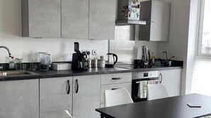 Eine moderne Küche mit grauen Schränken, einer schwarzen Arbeitsplatte, einer Kaffeemaschine und einem Wasserkocher.