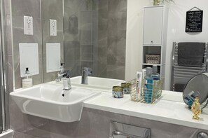 A modern bathroom with a white sink, two faucets, a mirror, and a towel rack. - Modern Apartment All Amenities Greater London (Rainham)