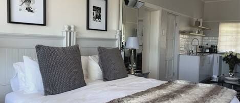 A hotel room with a bed, a mirror, a bedside table, and a view of the kitchen.