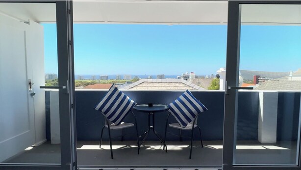 A balcony with two chairs and a small table, overlooking a cityscape. - 21 Cheviot Place (Cape Town)