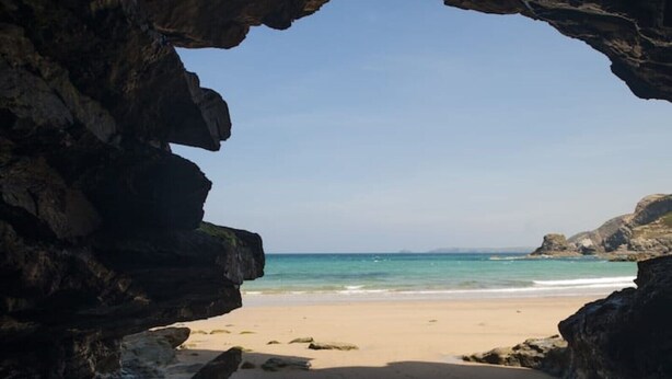 A beach view through a natural rock arch with clear blue water and sandy shore. - Gargoyle Cottage (St Agnes)