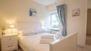 A neatly arranged bedroom with a bed, bedside tables, and a window with curtains. - Gargoyle Cottage (St Agnes)