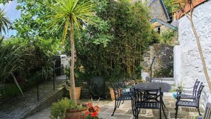 A patio with stone flooring, a round table, and black metal chairs. - Gargoyle Cottage (St Agnes)