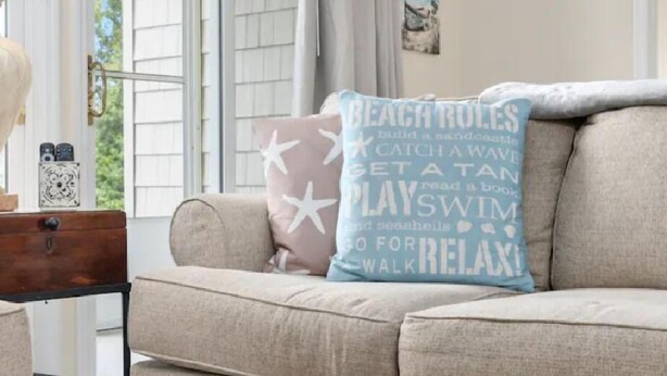 A living room with a beige sofa, a blue pillow with beach-related words, a wooden side table, and a book. - Fairway Dunes 2 BR Condo w/ Private lockout unit, Pool, Golf, Medical Center (Little River)