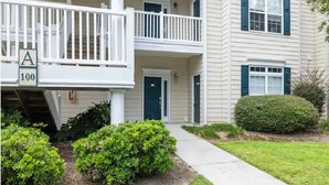 A two-story building with a front porch, a green door, and a sign indicating the address. - Fairway Dunes 2 BR Condo w/ Private lockout unit, Pool, Golf, Medical Center (Little River)