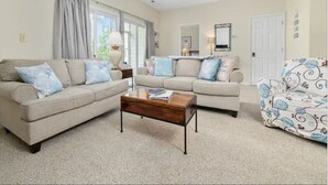 A living room with two sofas, a coffee table, a patterned armchair, a ceiling fan, and a window with curtains. - Fairway Dunes 2 BR Condo w/ Private lockout unit, Pool, Golf, Medical Center (Little River)
