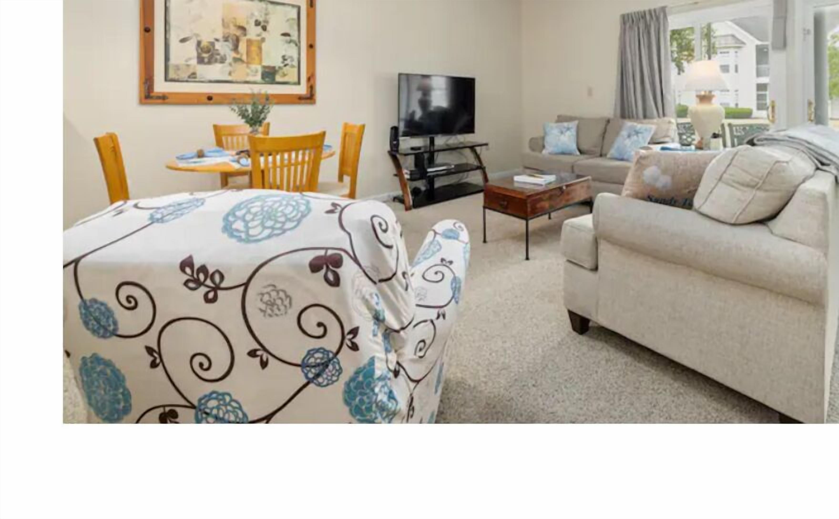 A living room with a sofa, a TV, a dining table with chairs, and a painting on the wall.