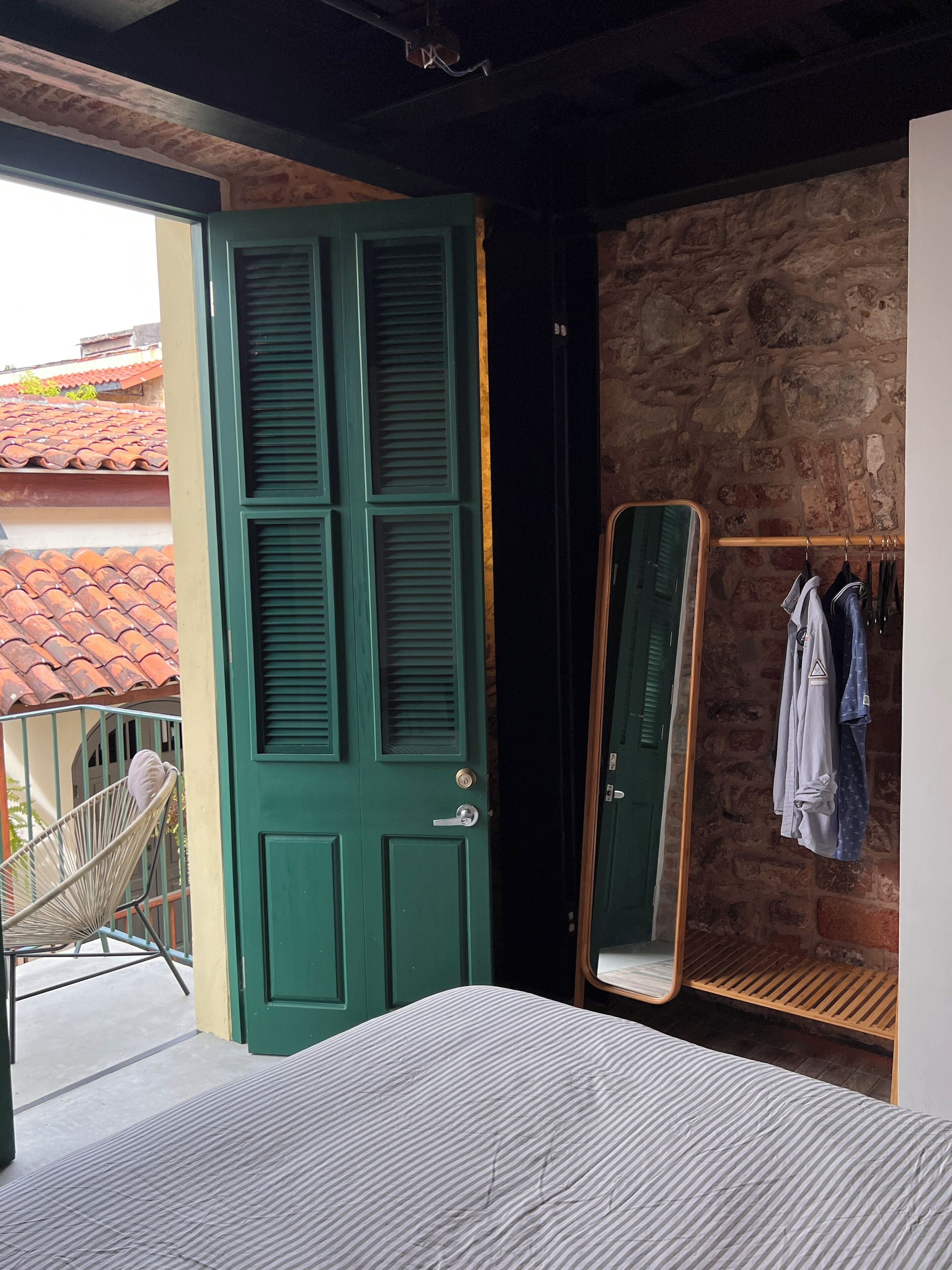 A room with a green door, a bed, a chair, a mirror, and a clothing rack.