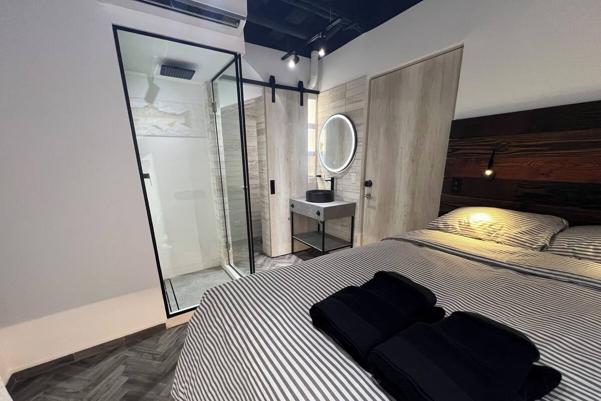 Un dormitorio moderno con una cama grande, una mesita de noche, un espejo y un vestidor con puerta corredera.