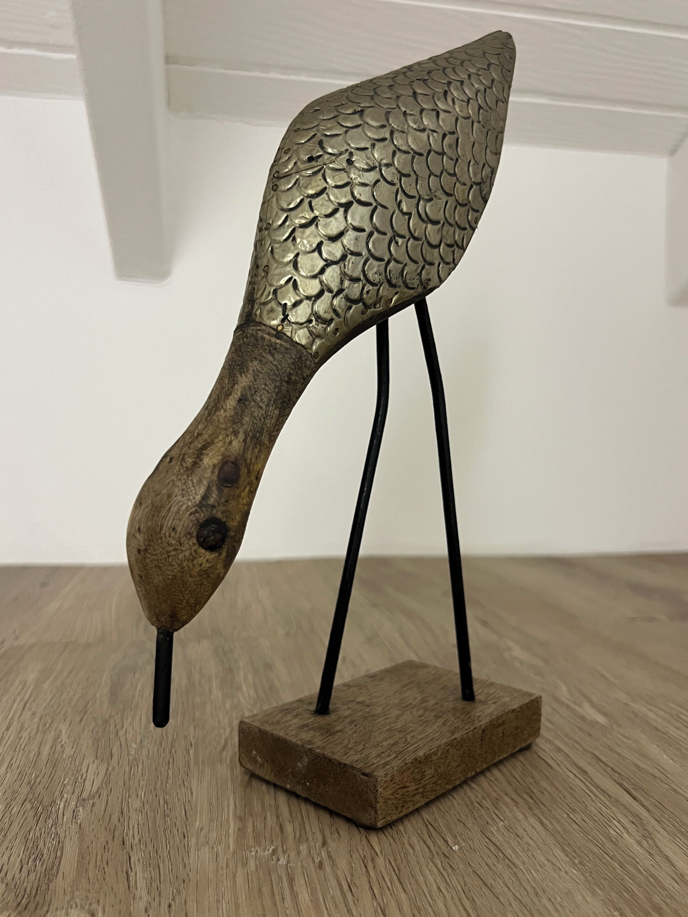 A decorative bird sculpture with a textured metallic body and a wooden base.