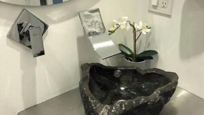 Un baño con un espejo grande, un lavamanos con un cuenco decorativo y una orquídea en maceta.