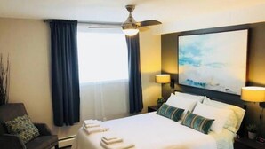 Una habitación de hotel con cama, una silla, ventilador de techo, un cuadro y dos lámparas.
