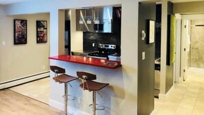 Una cocina moderna con encimera roja, electrodomésticos de acero inoxidable y dos taburetes de bar.