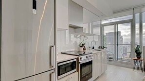 A modern kitchen with stainless steel appliances, a large window, and a balcony with a view of the city.