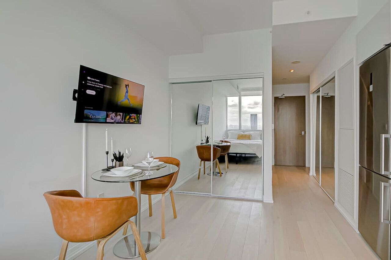 Habitación de hotel moderna con zona de comedor, televisor montado en la pared y un espejo grande que refleja la habitación.