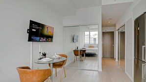 A modern hotel room with a dining area, a TV mounted on the wall, and a large mirror reflecting the room.