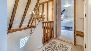 Eine Treppe mit freiliegenden Holzbalken, einem Chandelier und Blick in ein Schlafzimmer mit Bett und Nachttisch.