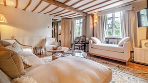 Ein gemütliches Zimmer mit einem Bett, einem Sofa, einem Tisch und einem Sessel. Es gibt ein Fenster mit Vorhängen und eine Heizung.