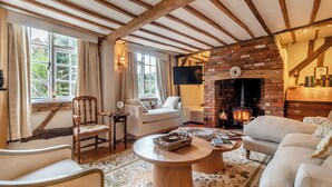 A cozy living room with exposed wooden beams, a brick fireplace, and comfortable seating. - 3 bedroom accommodation in Saffron Walden (Saffron Walden)