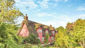 Ein traditionelles rotes Haus mit einem Strohdach, umgeben von üppiger Vegetation und Bäumen.