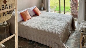 Une chambre avec un grand lit, un luminaire suspendu, une vue sur l’extérieur et un panier fixé au mur, orné d’une inscription.